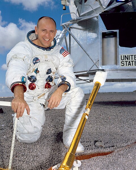 A color photograph showing Bean wearing his astronaut's space suit and kneeling in front of the lunar command module.